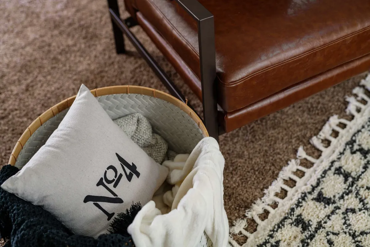 An inviting seating area with a leather chair, a basket holding a pillow, and a textured rug creates a comfortable nook. The warm, intimate setting is ideal for quiet conversations or simply enjoying a glass of wine after an evening walk.