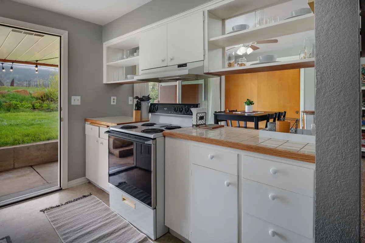 A bright kitchen featuring a modern stove, open shelving, a spacious kitchen island, and a doorway that hints at flow to the outdoors. The space is staged for cooking and gatherings, capturing the kitchen’s brand-new, fully equipped appeal.