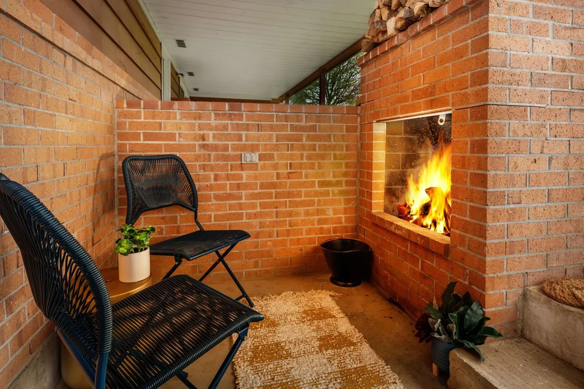 An inviting exterior patio space featuring a fireplace as the focal point, surrounded by comfortable chairs, a decorative rug, and potted plants. The setup exudes warmth and relaxation, providing a picturesque spot for guests to unwind outdoors while enjoying vineyard views.