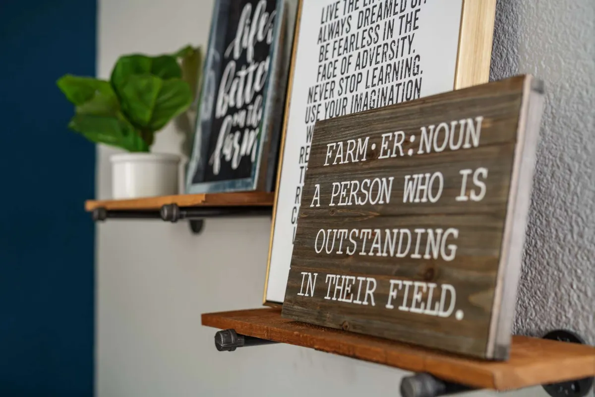 This image displays a thoughtfully decorated corner with a wooden sign providing a definition, framed inspirational quotes, and a lush green potted plant. The decor creates a motivational and uplifting vibe, making guests feel at ease and welcome.