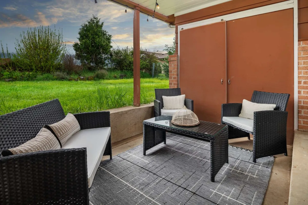 A cozy outdoor seating area on a sunken patio, complete with cushioned chairs, a decorative rug, a coffee table, and a well-kept green lawn. The setup is perfect for relaxing or entertaining, with the surrounding natural environment visible. The scene suggests comfort and connection to the outdoors, ideal for enjoying morning coffee or sunset drinks.
