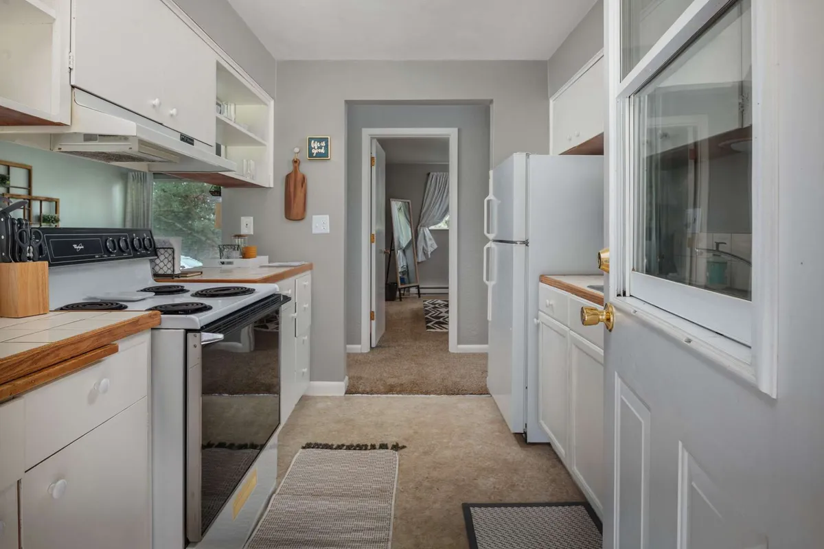 This image captures a bright and inviting kitchen area featuring a stove, sink, refrigerator, and a doorway leading into another room. The space feels cozy yet practical, suggesting an environment where guests can gather for meal preparation or enjoy quality time together in between event celebrations.