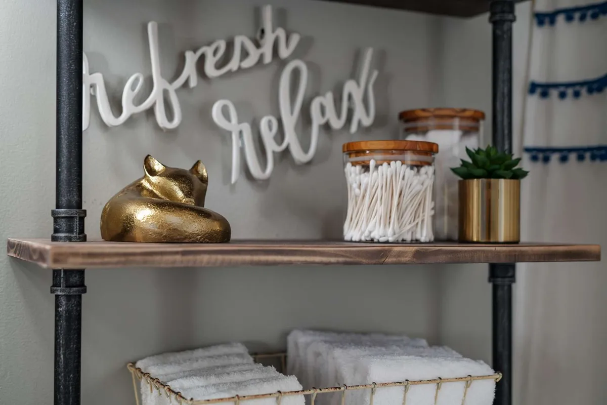 A calming bathroom vignette with a golden fox figurine, a 'refresh relax' sign, glass jars with cotton swabs, a green plant in a gold pot, and neatly stacked towels on display. The details enhance the sense of tranquility and self-care, reflecting a thoughtful approach to hospitality.